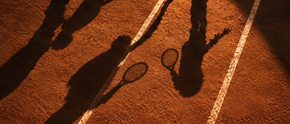 Imagem editorial com sombras de jogadores e raquetes sobre o saibro.